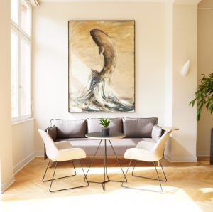 Neu gestaltetes, lichtdurchflutetes Foyer mit moderner Möblierung: Dunkelbraune Couch vor einer Wand, davor ein Beistelltisch mit einer Topfpflanze, zwei Stühlen. Über der Couch ist ein Gemälde mit einem Wal zu sehen.